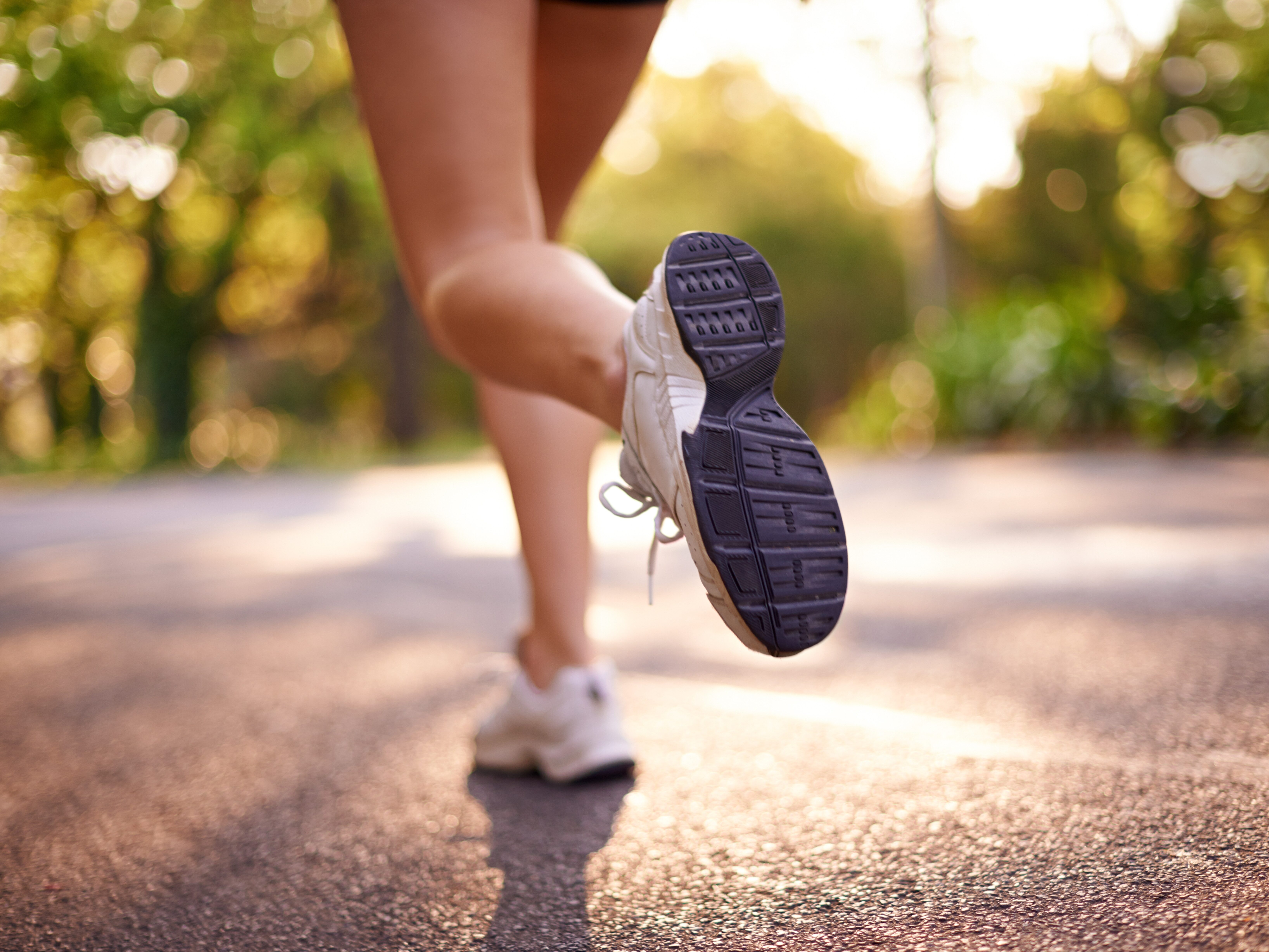 RunningLegsAndFitnessWithBackOfWomanInRoad - HASEBLO 平坦な道を走るイメージ